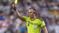 Soccer referee in a lime green jersey holds up a yellow card, signaling a foul during a match.