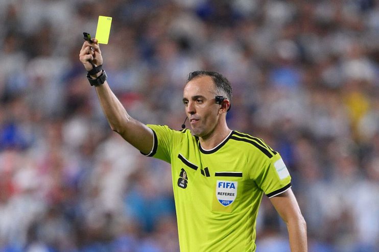 Soccer referee in a lime green jersey holds up a yellow card, signaling a foul during a match.