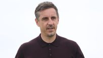 Gary Neville in a dark polo shirt, looking slightly to the right, against a clear sky.