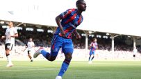 Footballer in a blue and red jersey running on a green field during a sunny match.