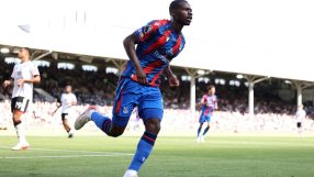 Footballer in a blue and red jersey running on a green field during a sunny match.