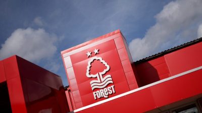 Nottingham Forest FC logo and club building exterior, red facade with white tree emblem and two stars against blue sky.
