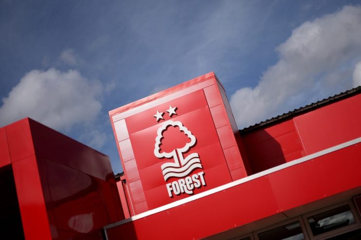 Nottingham Forest FC logo and club building exterior, red facade with white tree emblem and two stars against blue sky.