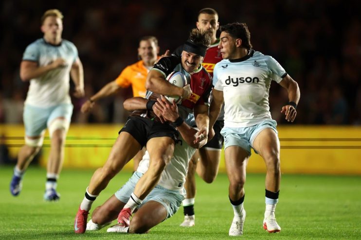 Rugby player in brown and red jersey being tackled by opponent in light blue jersey on green field