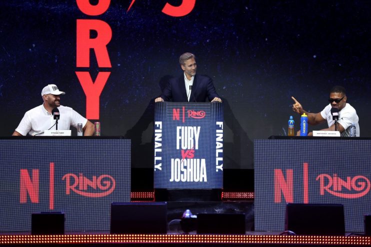Tyson Fury, a man in a suit, and Anthony Joshua at a press conference for the Fury vs. Joshua fight.