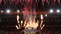 Rugby team celebrating Betfred Super League Grand Final victory with fireworks and flames on field.