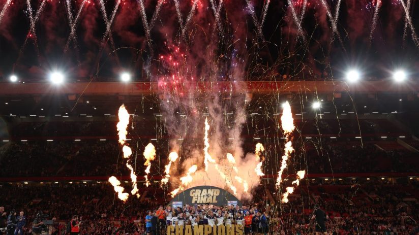 Rugby team celebrating Betfred Super League Grand Final victory with fireworks and flames on field.