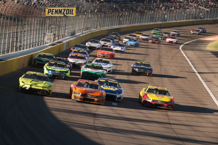 NASCAR stock cars racing on an oval track, with a yellow Pennzoil sign visible above the track.