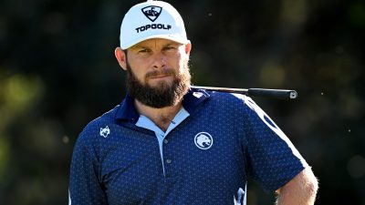 Bearded man in white Topgolf hat and blue patterned polo shirt, golf club on shoulder.