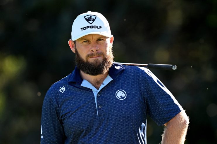 Bearded man in white Topgolf hat and blue patterned polo shirt, golf club on shoulder.