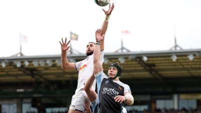 Rugby players leaping for a lineout ball during a match, stadium crowd in background