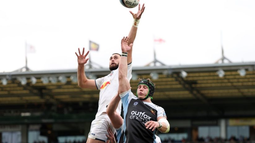 Rugby players leaping for a lineout ball during a match, stadium crowd in background