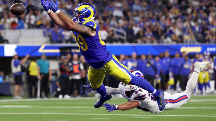 Rams player in blue and yellow uniform leaps to catch a football over a Bills player on the ground