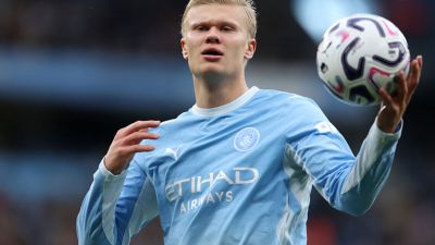 Erling Haaland in Manchester City light blue jersey holding a football, looking forward on the field