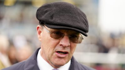 Man in a dark flat cap and sunglasses speaking, wearing a white shirt and patterned purple tie.