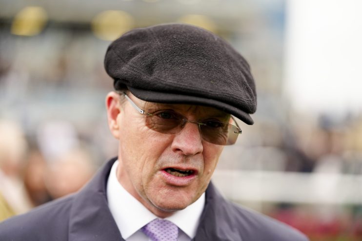 Man in a dark flat cap and sunglasses speaking, wearing a white shirt and patterned purple tie.