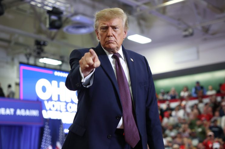 Donald Trump points at a political rally with an OHIO VOTE ON sign in the background.