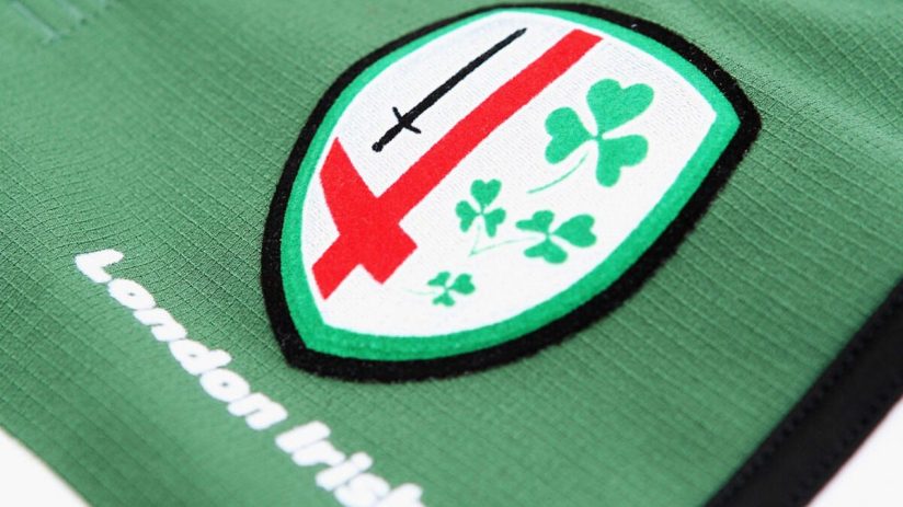 Close-up of the London Irish rugby club logo on a green jersey, featuring a sword, red cross, and shamrocks.