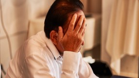 Distressed man in a white shirt covering his face with his hand, showing stress or disappointment.