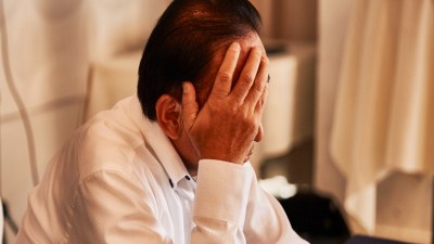 Distressed man in a white shirt covering his face with his hand, showing stress or disappointment.