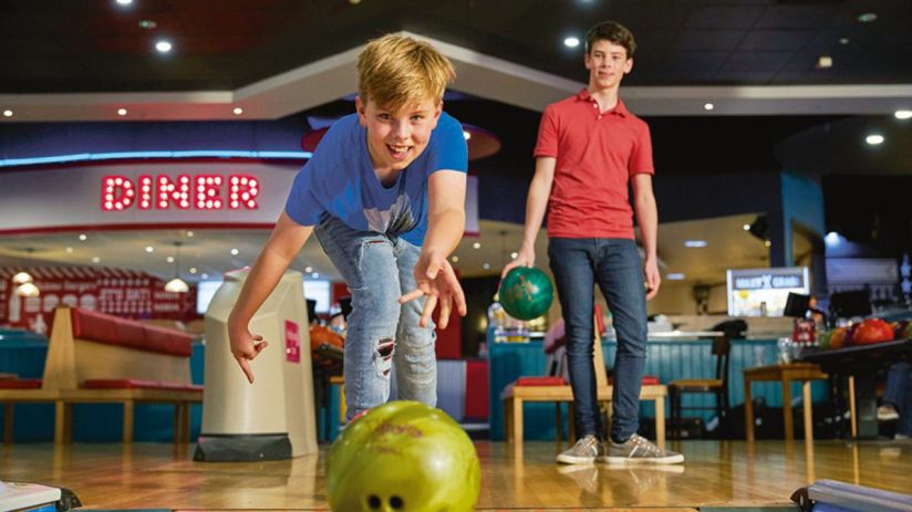 Two boys bowling at Hollywood Bowl, one rolling a green ball, the other holding a green ball.