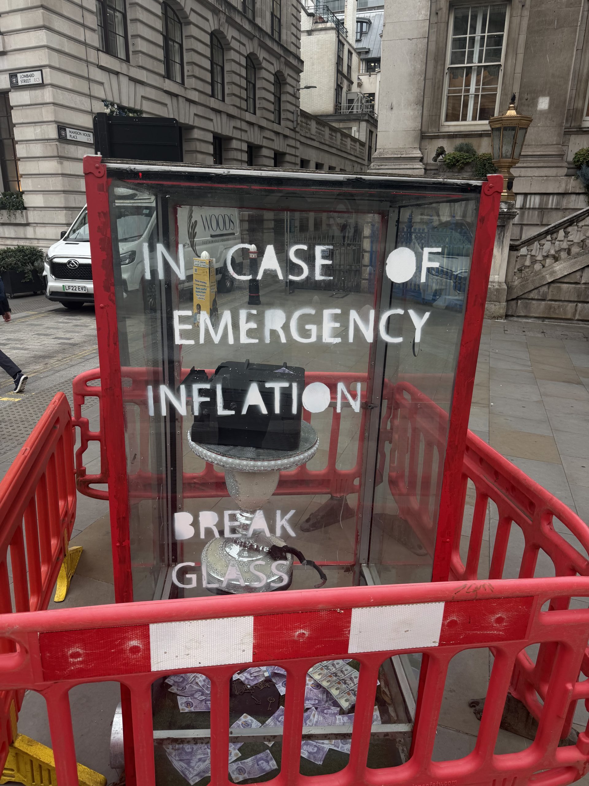 In Case of Emergency Break Glass box for inflation, containing money and a disco ball, on a city street.