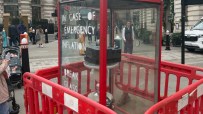 Emergency inflation display with Break Glass instructions, printer inside, surrounded by red barriers on a city street.