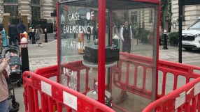 Emergency inflation display with Break Glass instructions, printer inside, surrounded by red barriers on a city street.