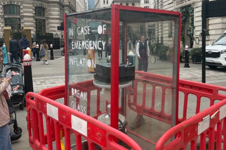 Emergency inflation display with Break Glass instructions, printer inside, surrounded by red barriers on a city street.