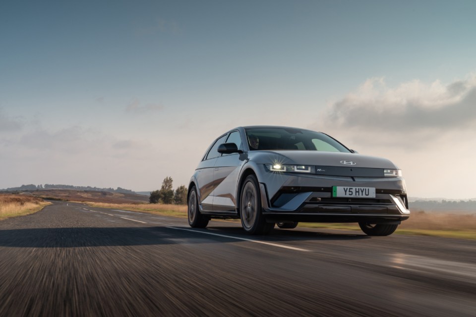 Gray Hyundai Ioniq 5 electric car driving on a rural road with blurred motion, under a cloudy sky.