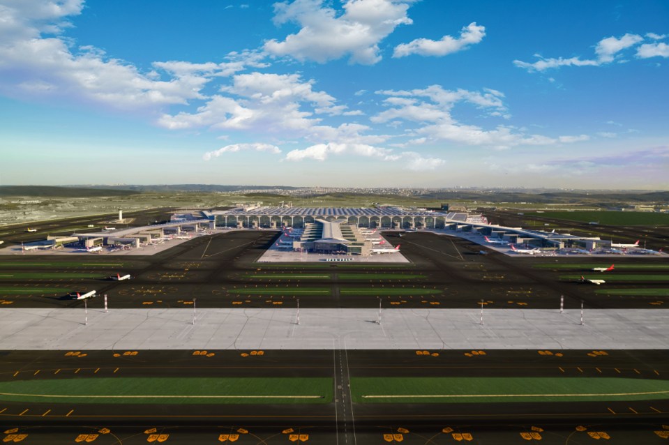 Aerial view of a large, modern Istanbul airport terminal with multiple aircraft on the tarmac under a blue sky.