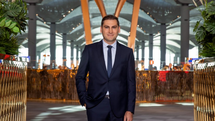 Istanbul Airport CEO Kadri Samsunlu in a dark suit and tie, standing inside the modern airport terminal.