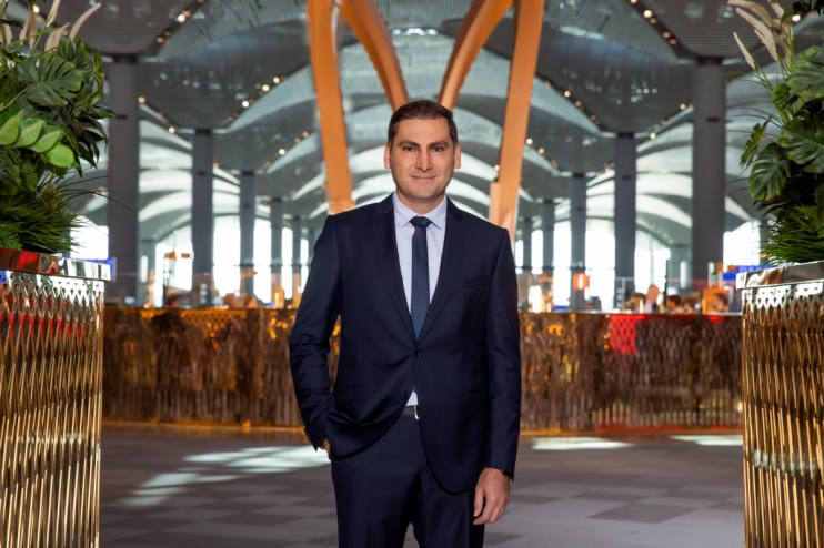 Istanbul Airport CEO Kadri Samsunlu in a dark suit and tie, standing inside the modern airport terminal.