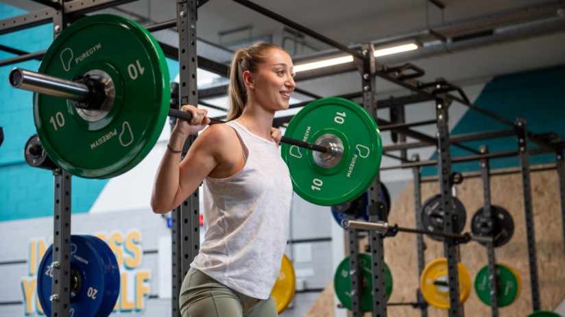Woman squatting with a barbell and green PureGym weight plates in a modern gym facility