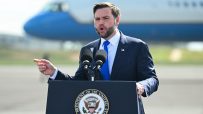 JD Vance speaking at a podium with the Vice Presidents seal, pointing, with a plane in the background.
