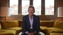 Jim ONeill, economist and former Goldman Sachs chairman, seated on a mustard velvet sofa in front of large windows.