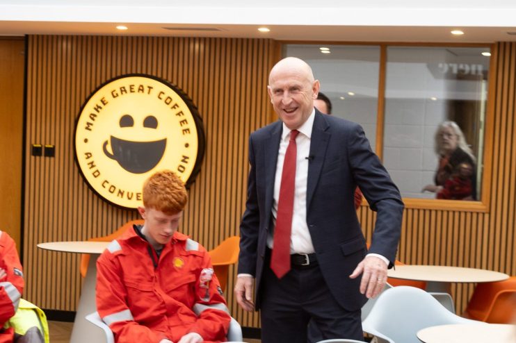 John Healey, MP, speaking with workers in orange overalls at a gas terminal.
