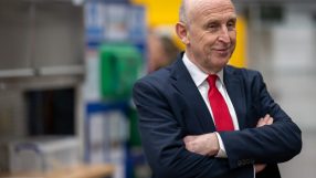 Chancellor John Healey in a dark suit and red tie, arms crossed, smiling.