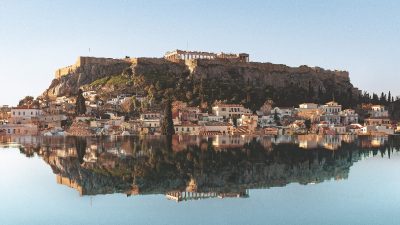 Acropolis of Athens and historic Plaka neighborhood reflected in calm water, ideal literary stay in Greece.
