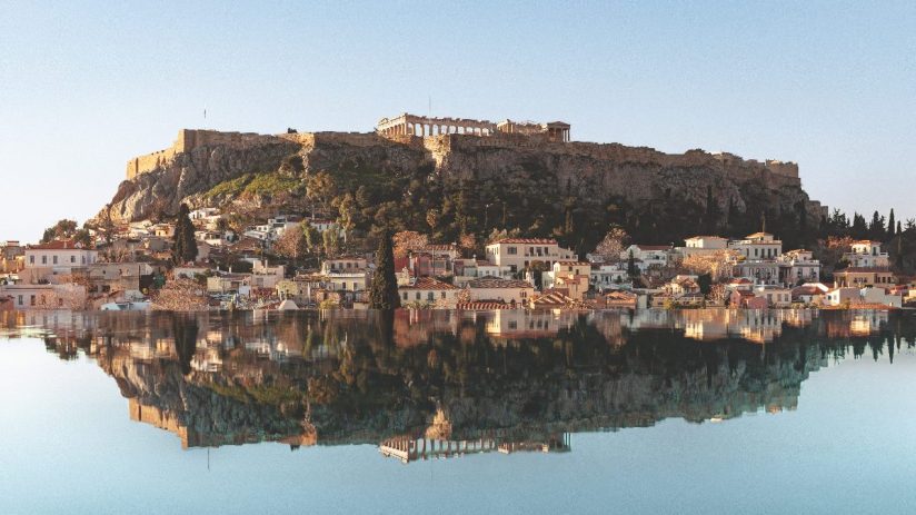 Acropolis of Athens and historic Plaka neighborhood reflected in calm water, ideal literary stay in Greece.
