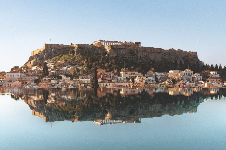 Acropolis of Athens and historic Plaka neighborhood reflected in calm water, ideal literary stay in Greece.
