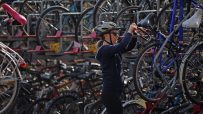Woman in helmet and sunglasses locking a bicycle to a full London bike rack