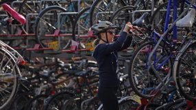 Woman in helmet and sunglasses locking a bicycle to a full London bike rack