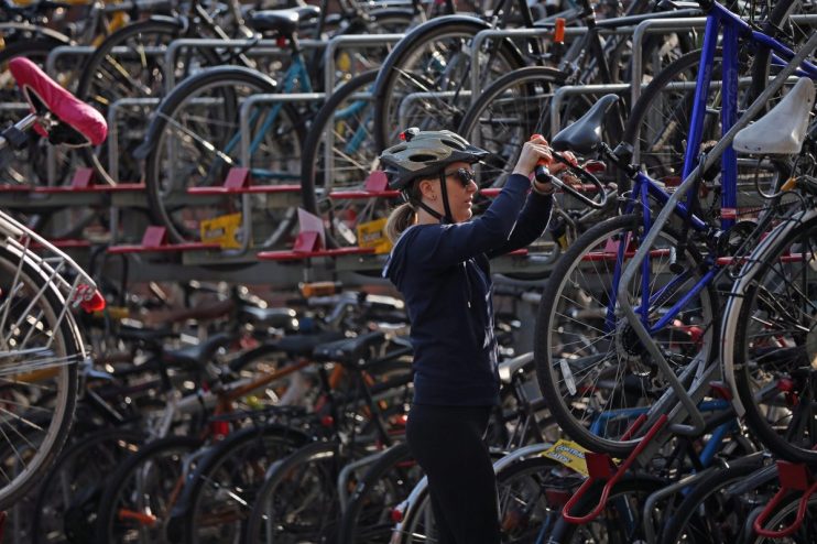 Woman in helmet and sunglasses locking a bicycle to a full London bike rack