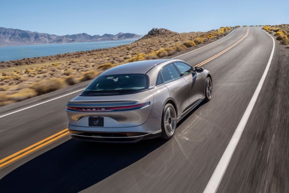 Silver Lucid Gravity electric SUV driving on a winding desert road beside a lake and mountains