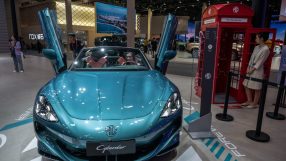 MG Cyberster electric roadster at an auto show, with a woman in the drivers seat and another by a red phone booth
