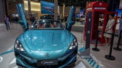 MG Cyberster electric roadster at an auto show, with a woman in the drivers seat and another by a red phone booth