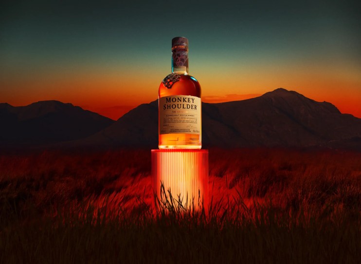 Monkey Shoulder blended malt Scotch whisky bottle on a glowing red pedestal at sunset