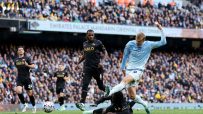 Manchester City player Erling Haaland in action during a football match, with other players and fans in the background.