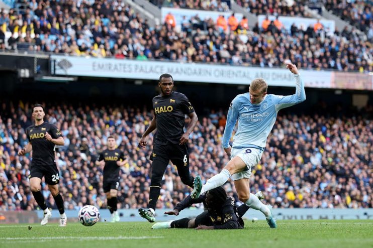 Manchester City player Erling Haaland in action during a football match, with other players and fans in the background.